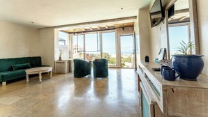 Ein geräumiges Wohnzimmer mit einem grünen Sofa, zwei Sesseln, einem Couchtisch und einem großen Fenster mit Blick auf die Stadt.