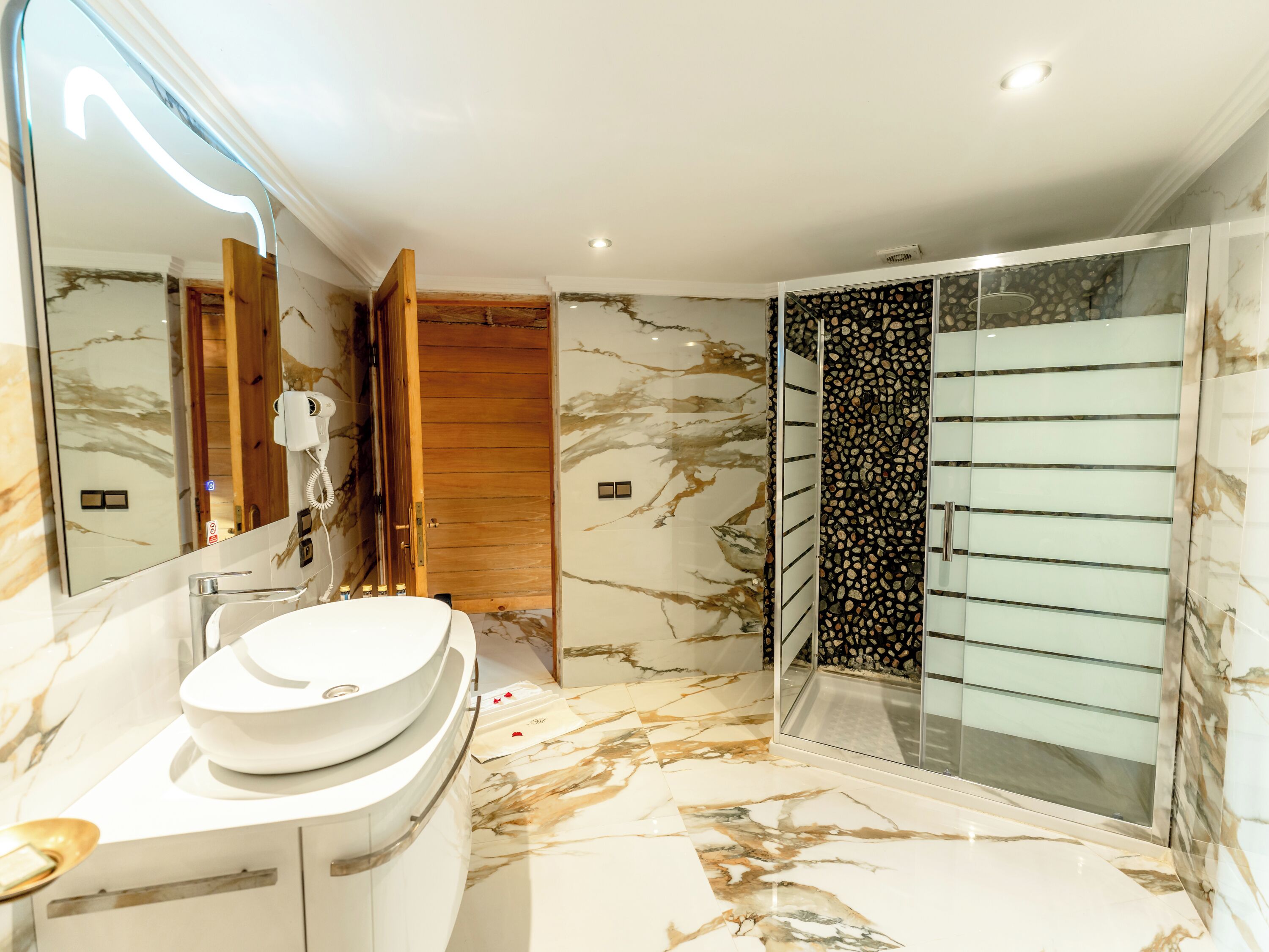 A modern bathroom with a marble floor, a large mirror, a sink, and a shower area.