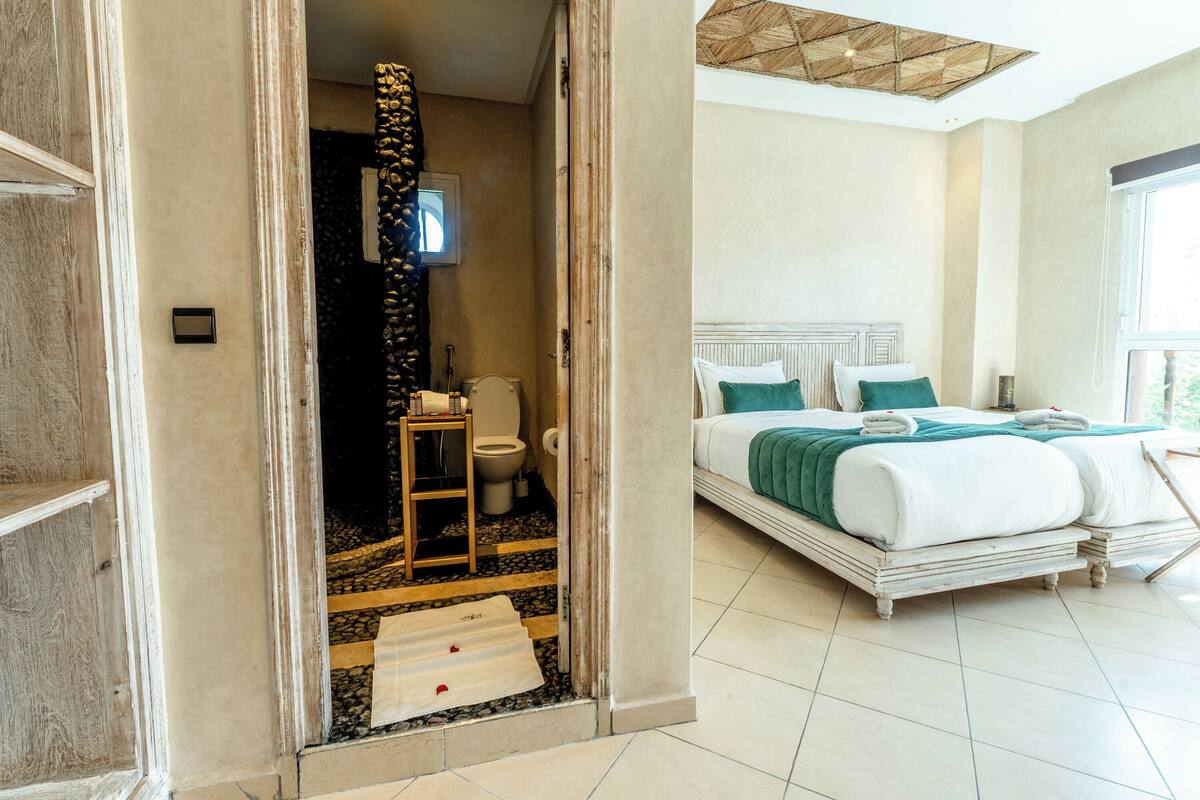 A hotel room with a large bed, a bathroom with a stone wall, and a wooden ladder leading to the shower.