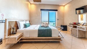 Ein modernes Hotelzimmer mit einem großen Bett, einem Fernseher, einer Minibar und einem Balkon mit Blick.