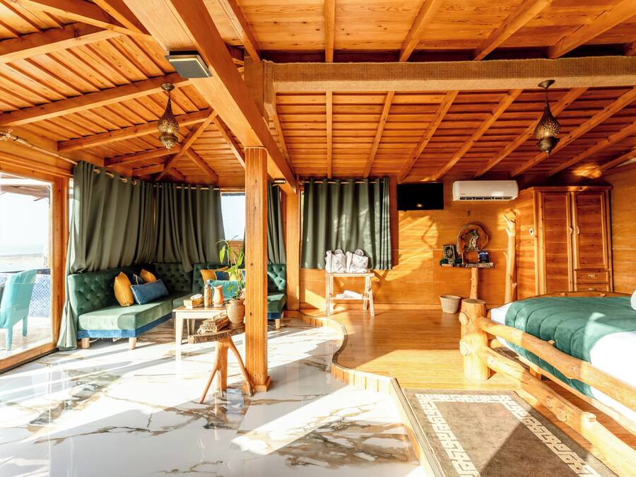 A wooden cabin interior with a bed, sofa, and dining area.