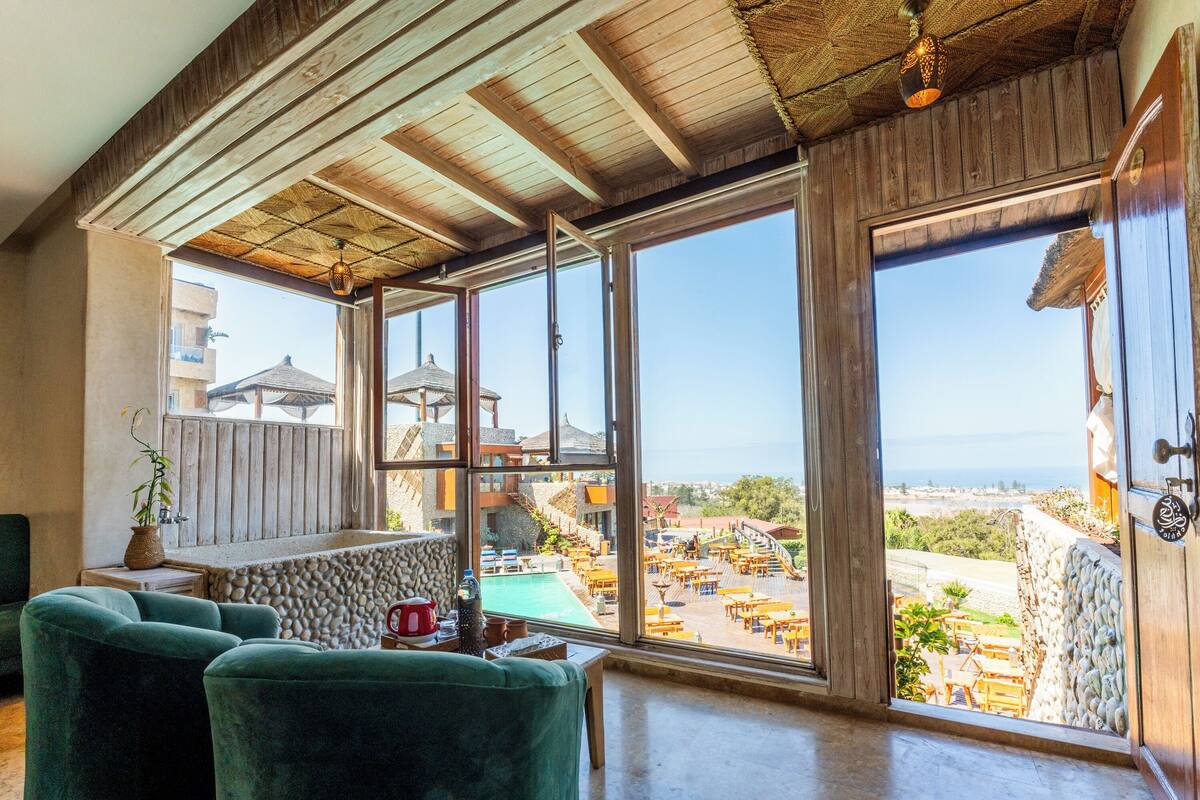 A room with a large window overlooking a pool and outdoor seating area.