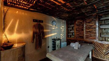 A room with a wooden ceiling, a bed with a white mattress, a wooden cabinet, and a wall clock.