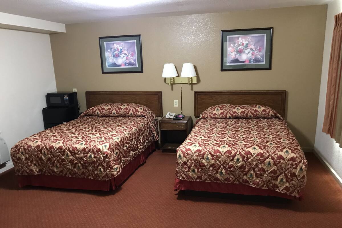 A hotel room with two beds, a nightstand with lamps, and two framed floral pictures on the wall.