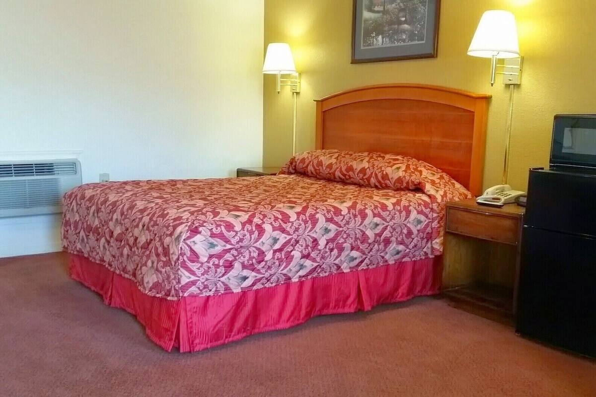 A hotel room with a bed, two bedside lamps, a heater, a telephone, and a television.