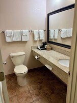 Un baño con inodoro, lavamanos y varias toallas colgadas en un perchero.