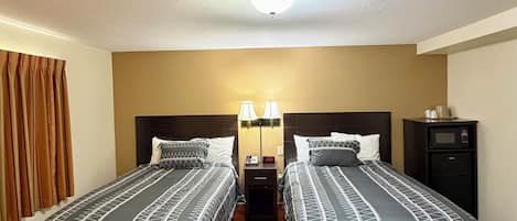 Una habitación de hotel con dos camas, una mesita de noche con lámparas, un reloj y un armario pequeño.