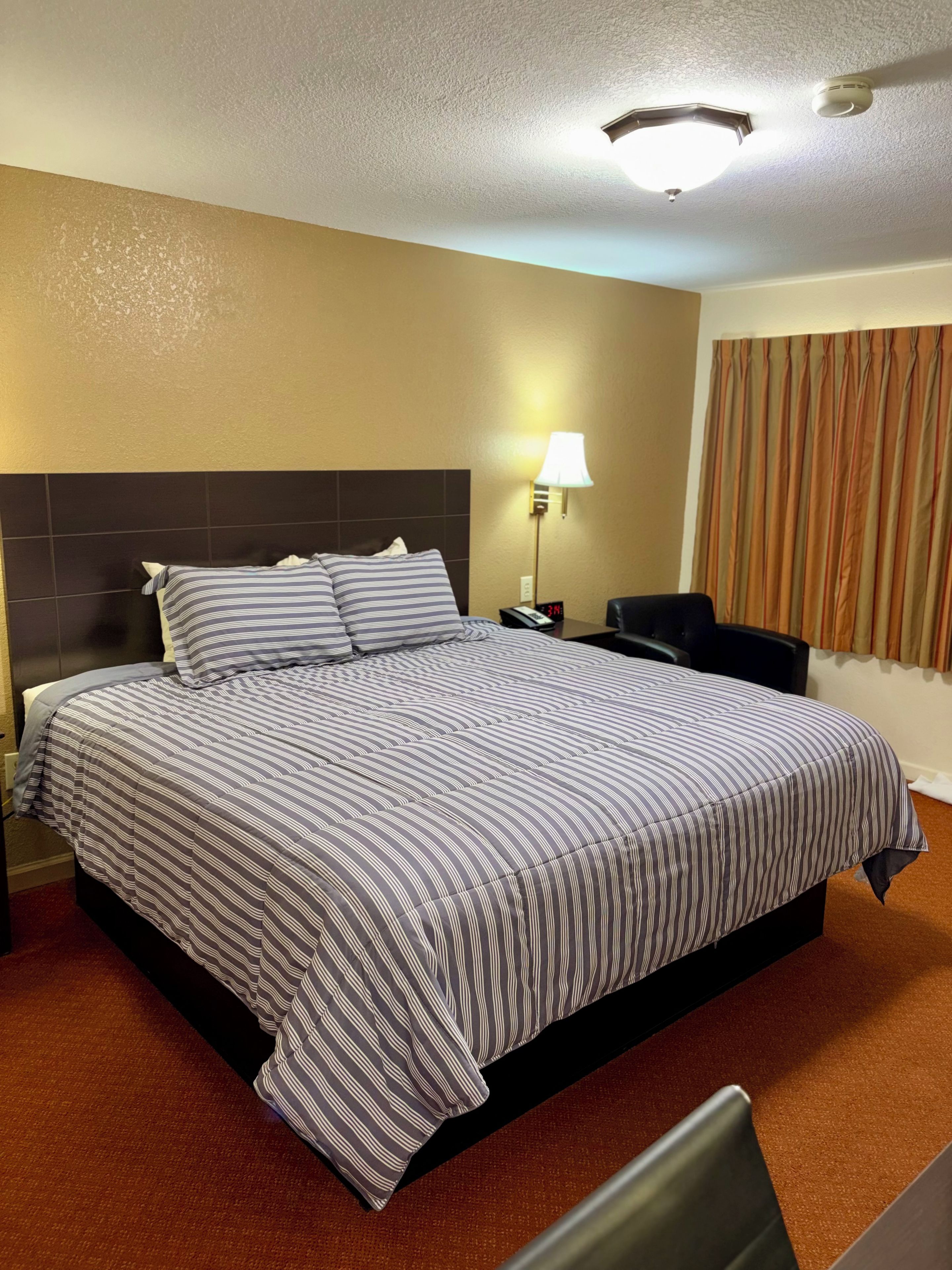 Habitación de hotel con una cama grande, una mesita de noche, una lámpara y vistas al exterior.
