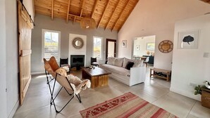 Uma sala de estar espaçosa com teto de madeira alto, lareira, sofá, mesa de centro e tapete estampado.