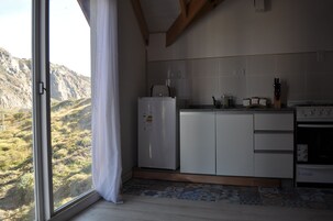 Una cocina con armarios blancos, un refrigerador, una estufa y una ventana con vista a un paisaje montañoso.