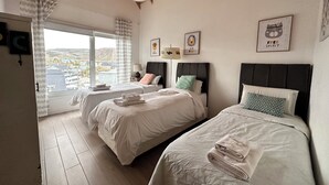 Quarto de hotel com duas camas, uma janela grande com vista e teto com vigas de madeira aparente.