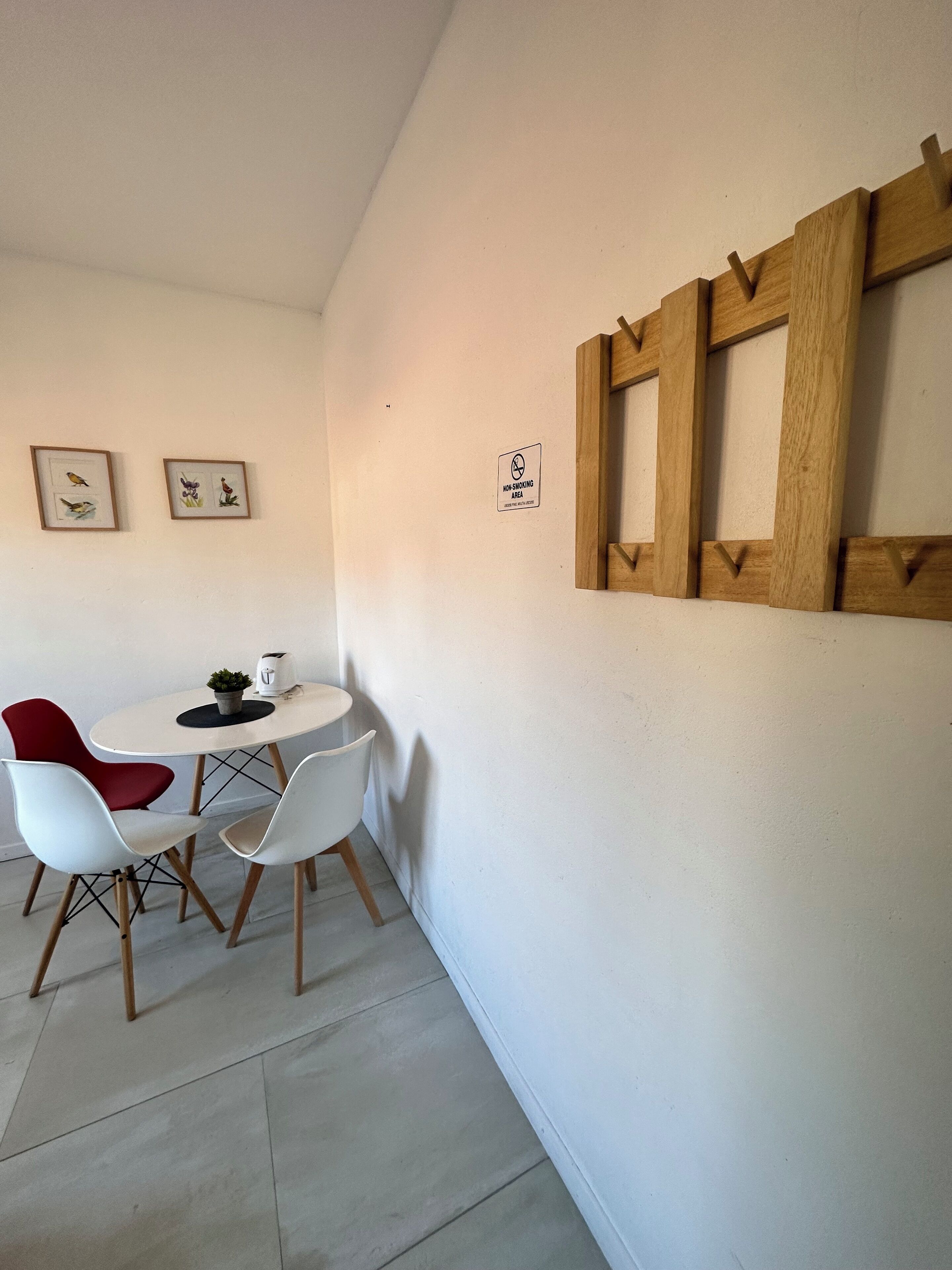 Un comedor con una mesa blanca y dos sillas, una roja y otra blanca. Hay cuadros en la pared y un cartel de prohibido fumar.