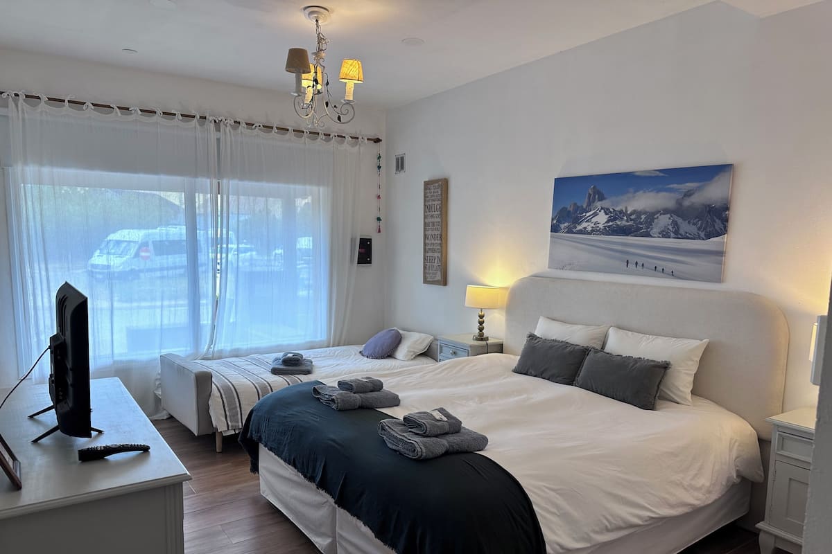 A hotel room with a large bed, a smaller bed, a desk with a TV, and a painting on the wall.