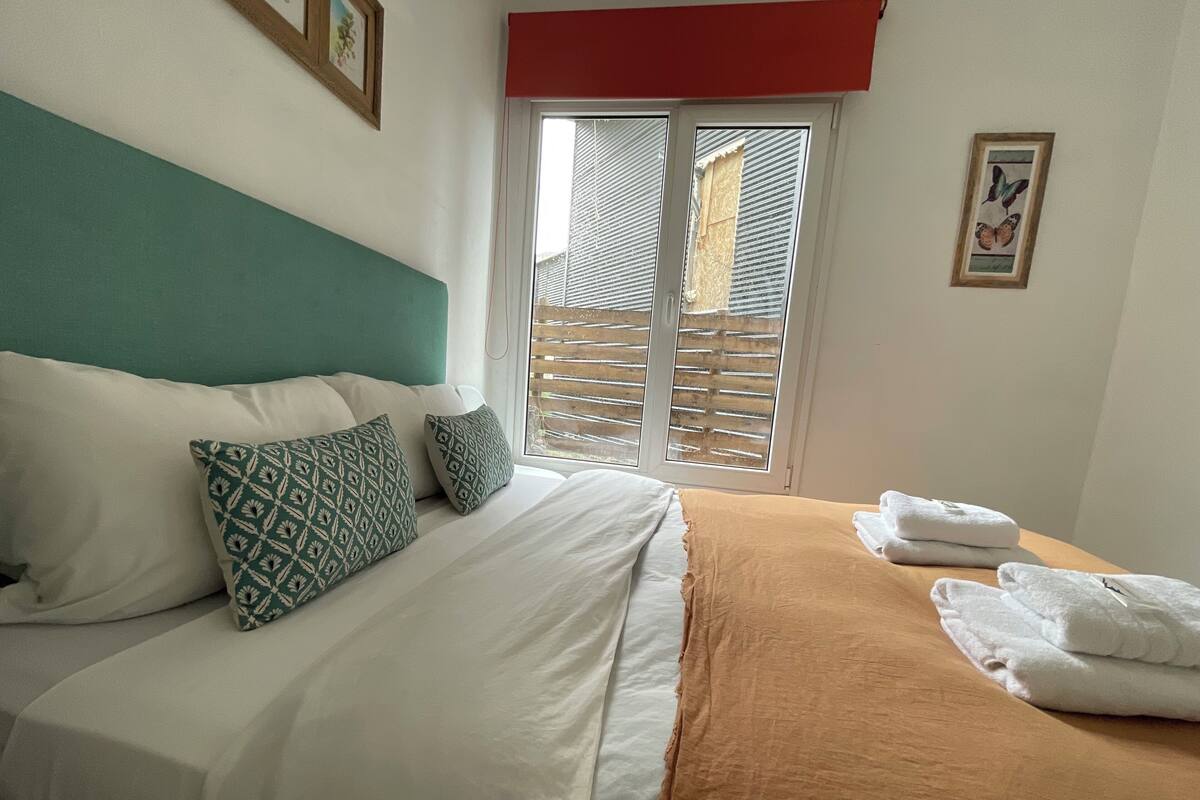 A hotel room with a bed, pillows, a window with blinds, and a towel on the bed.