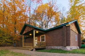 Une cabane en rondins dotée d’un porche, entourée d’arbres aux couleurs automnales.