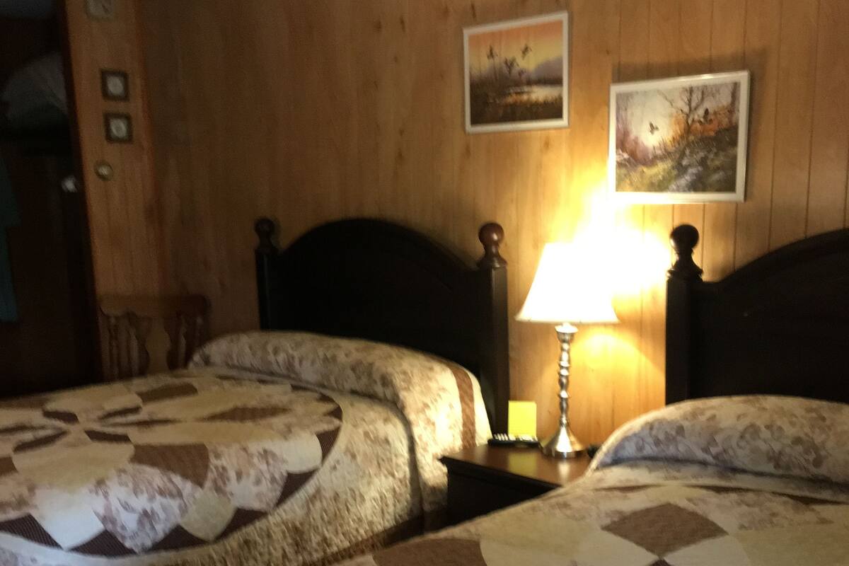 A hotel room with two beds, wooden paneling on the walls, and two framed pictures.