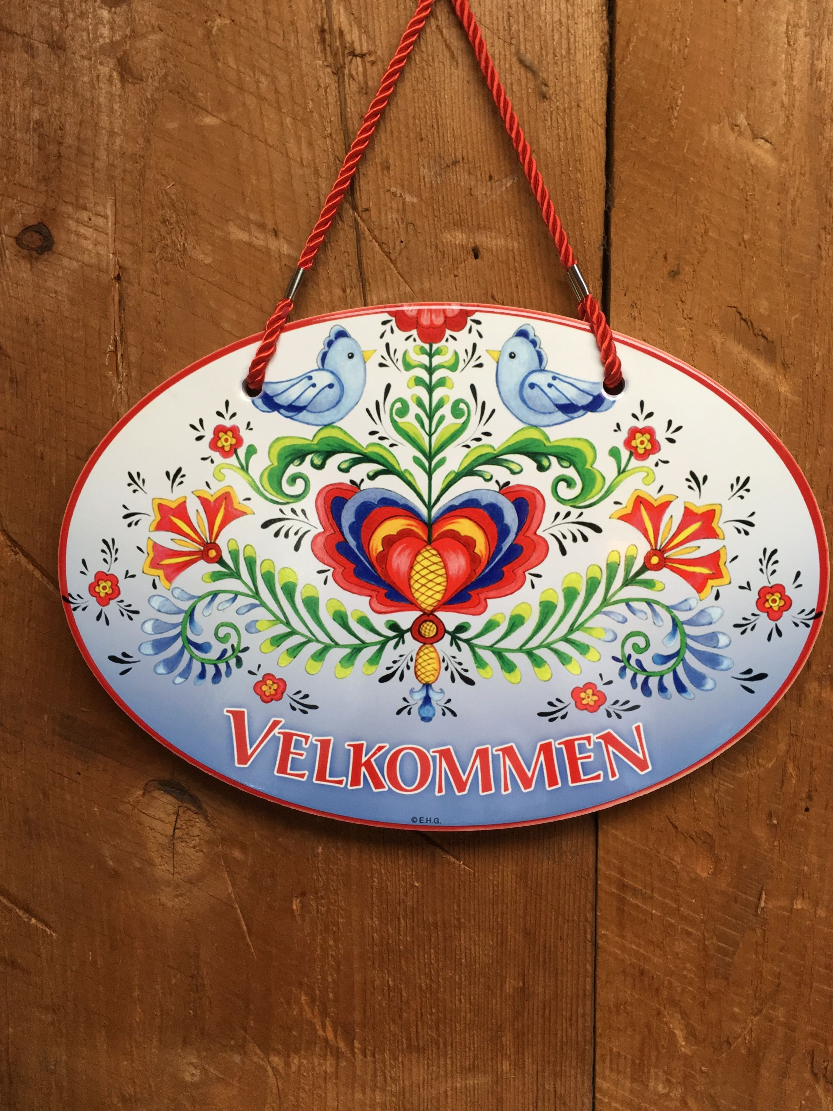 A colorful welcome sign with a bird design and the text "VELKOMMEN" on a wooden background.