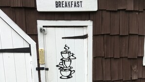 A white door with a sign reading "BREAKFAST" above it, a thermometer, and a drawing of stacked cups with steam. - Cave Mountain Motel (Windham)