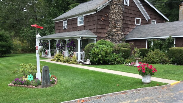 A two-story house with a stone chimney, a porch with flower boxes, and a well-maintained lawn. - Cave Mountain Motel (Windham)