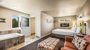 Habitación de hotel con una bañera grande, una cama, un televisor y una ventana con vistas a árboles.