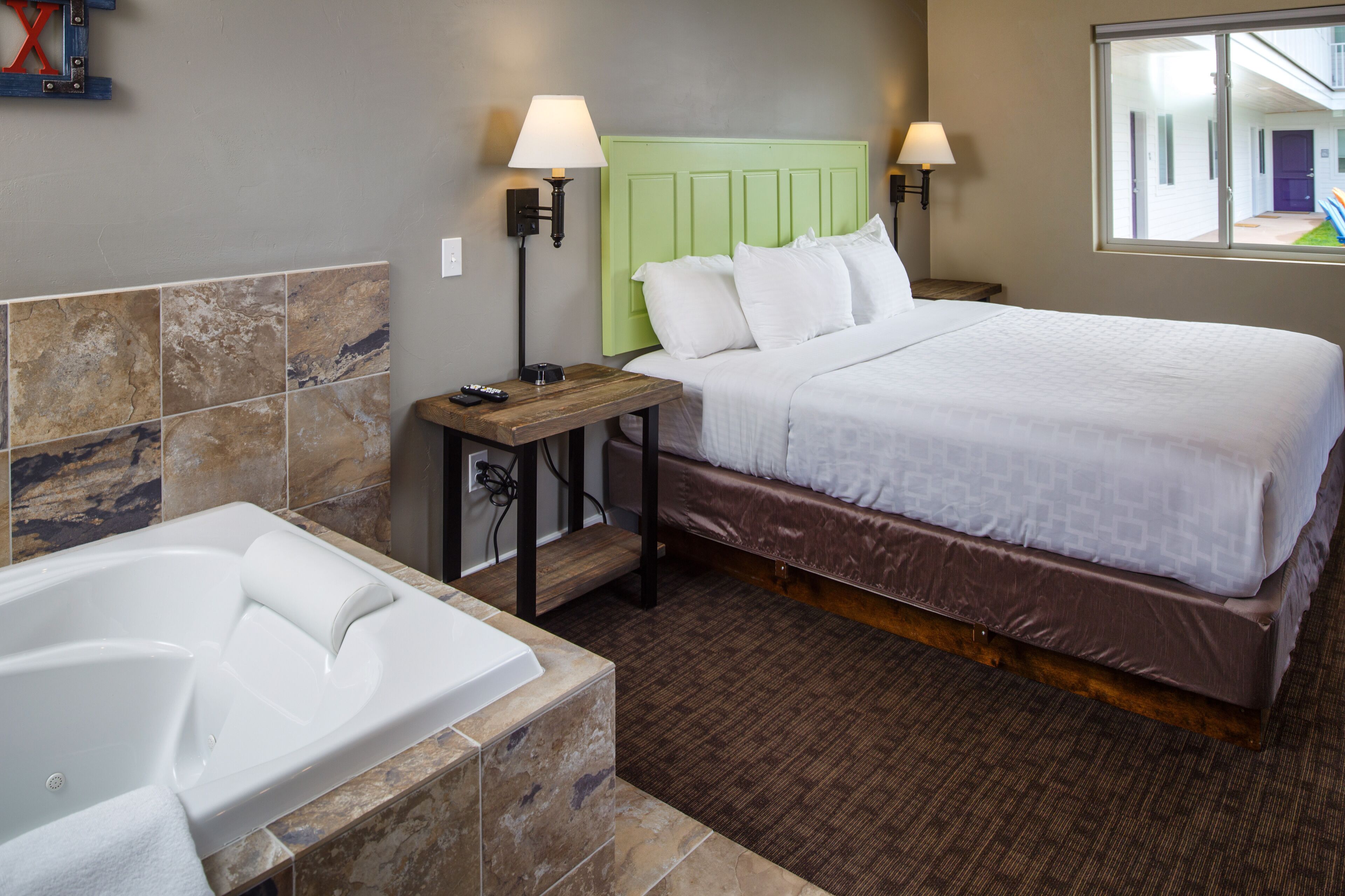 A hotel room with a large bed, a separate bathroom with a bathtub, and a window providing a view of the outside.