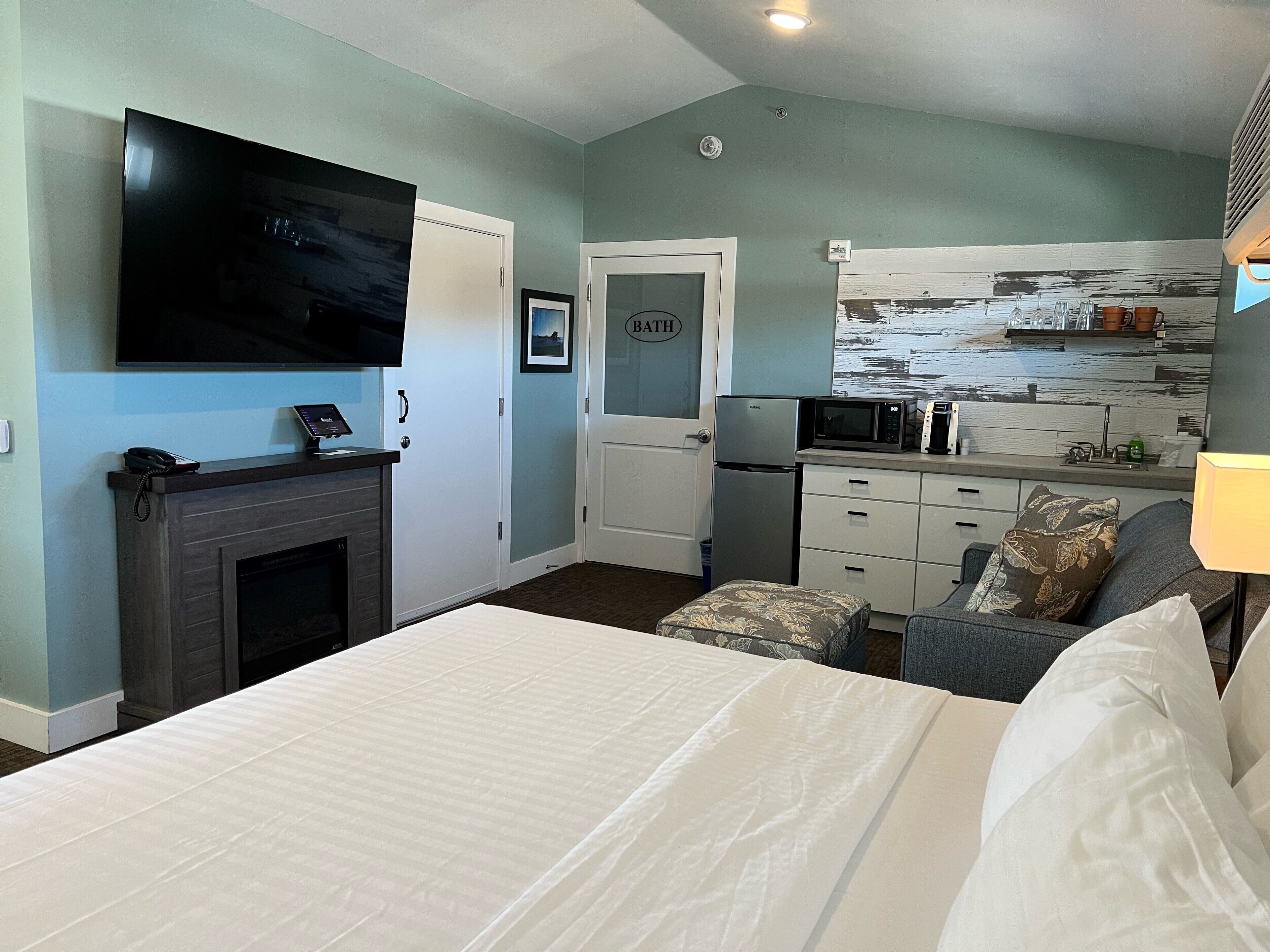Habitació d'hotel amb llit, televisió, petita cuina i bany.