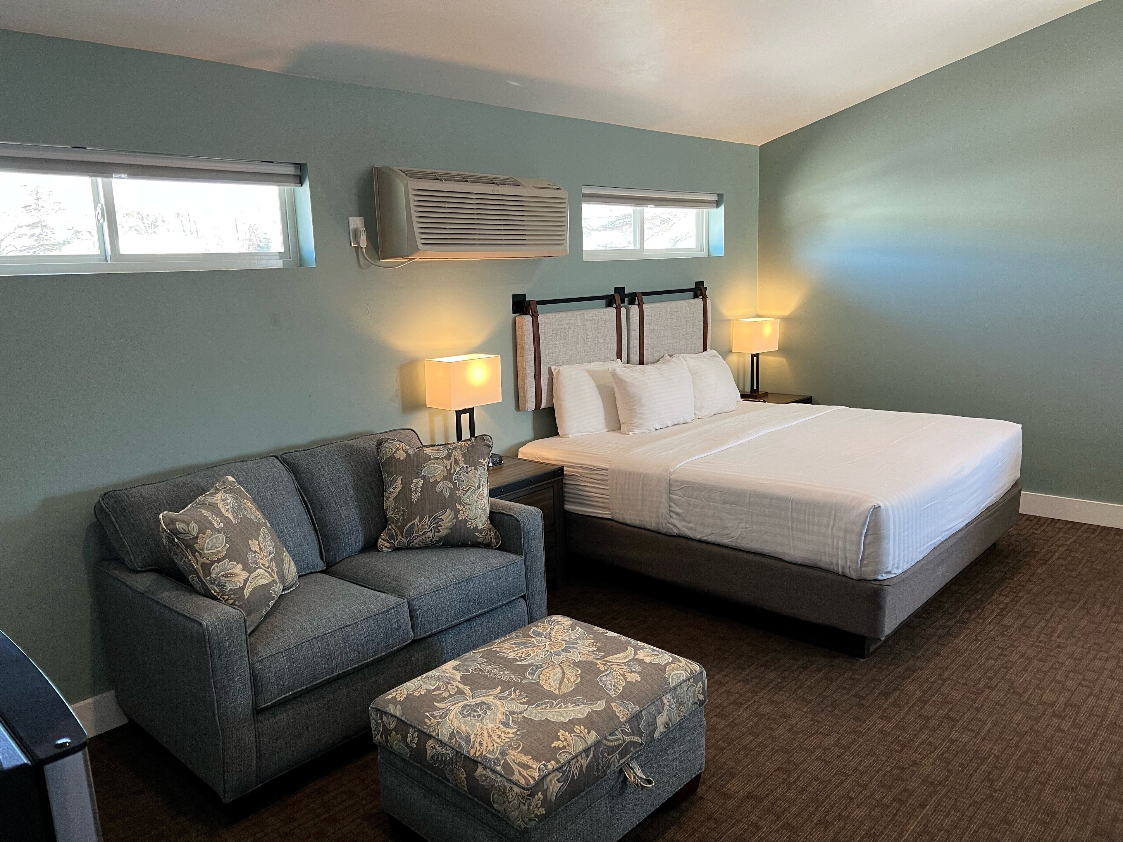Een slaapkamer met een bed, een slaapbank, een poef, twee bedlampen en een airconditioning.
