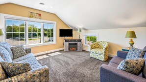 Ein Wohnzimmer mit Kamin, zwei Sofas, einem Fernseher und großen Fenstern mit Blick ins Freie.