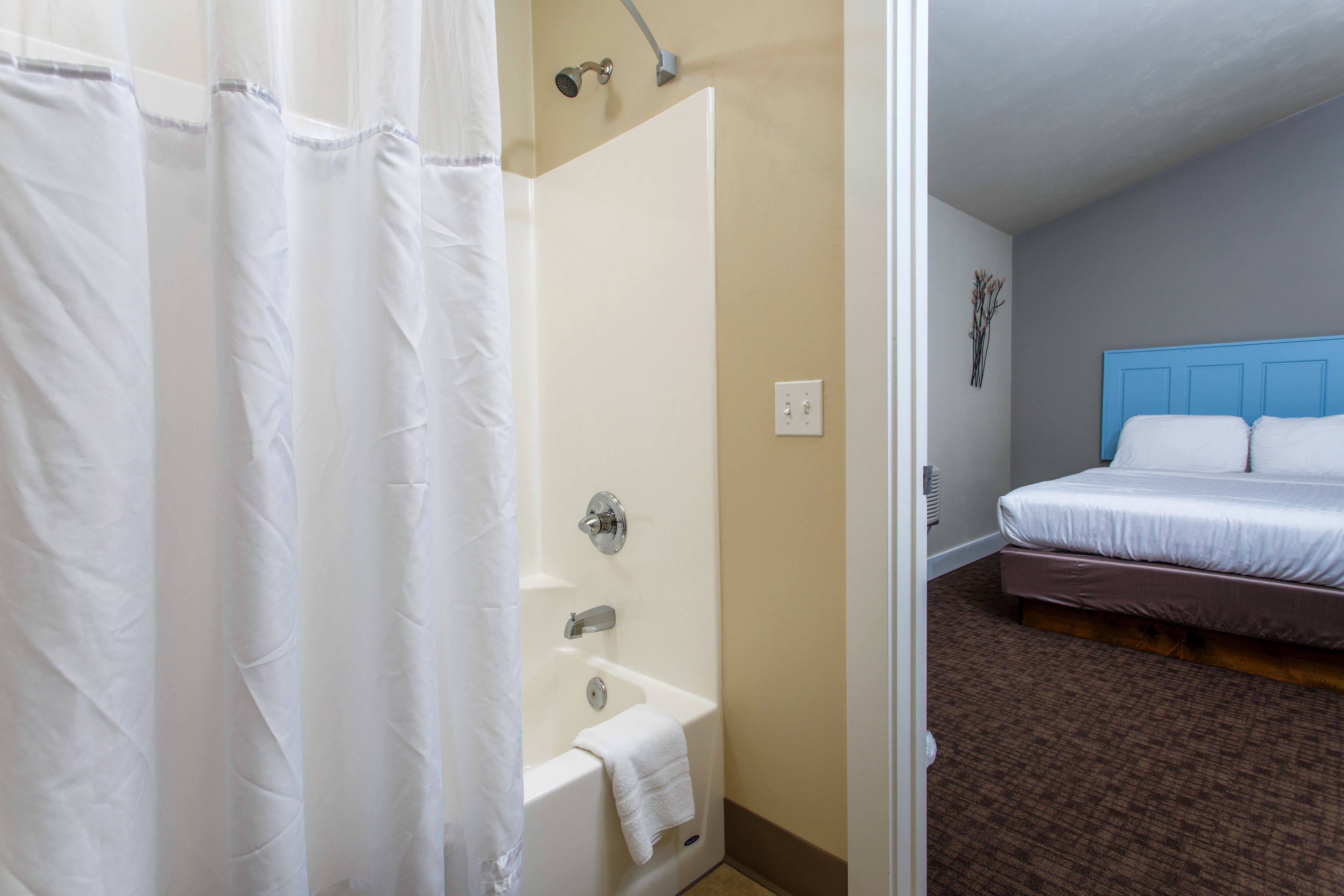 Une chambre d’hôtel avec une baignoire blanche, une tête de lit bleue et une moquette marron.