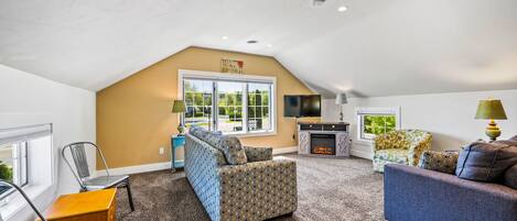 A spacious living room with a high ceiling, a fireplace, and a large window providing natural light.