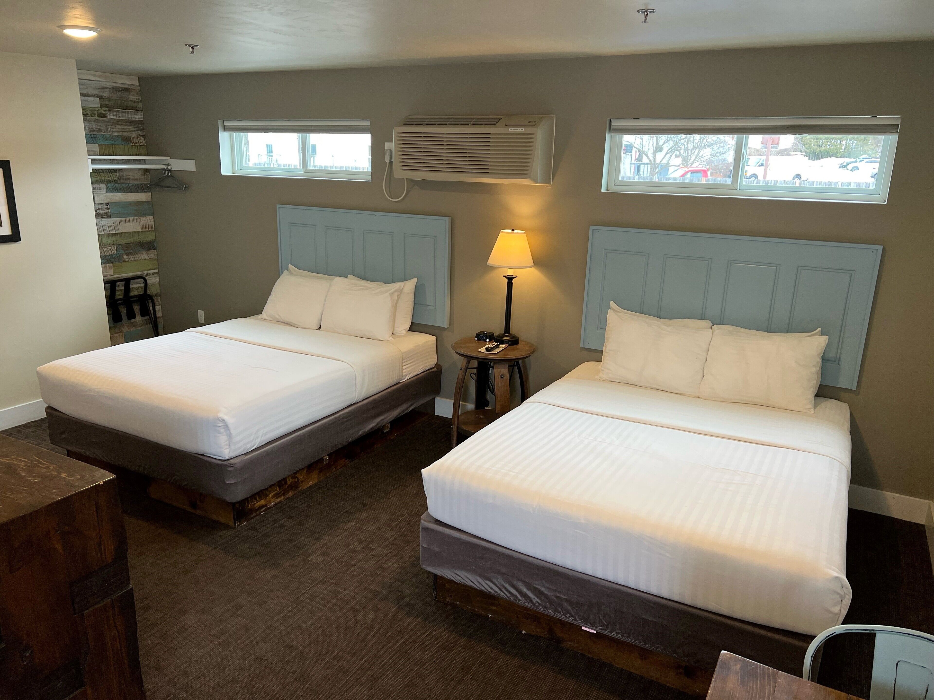 Two single beds with wooden headboards, a small bedside table with a lamp, and an air conditioning unit on the wall.