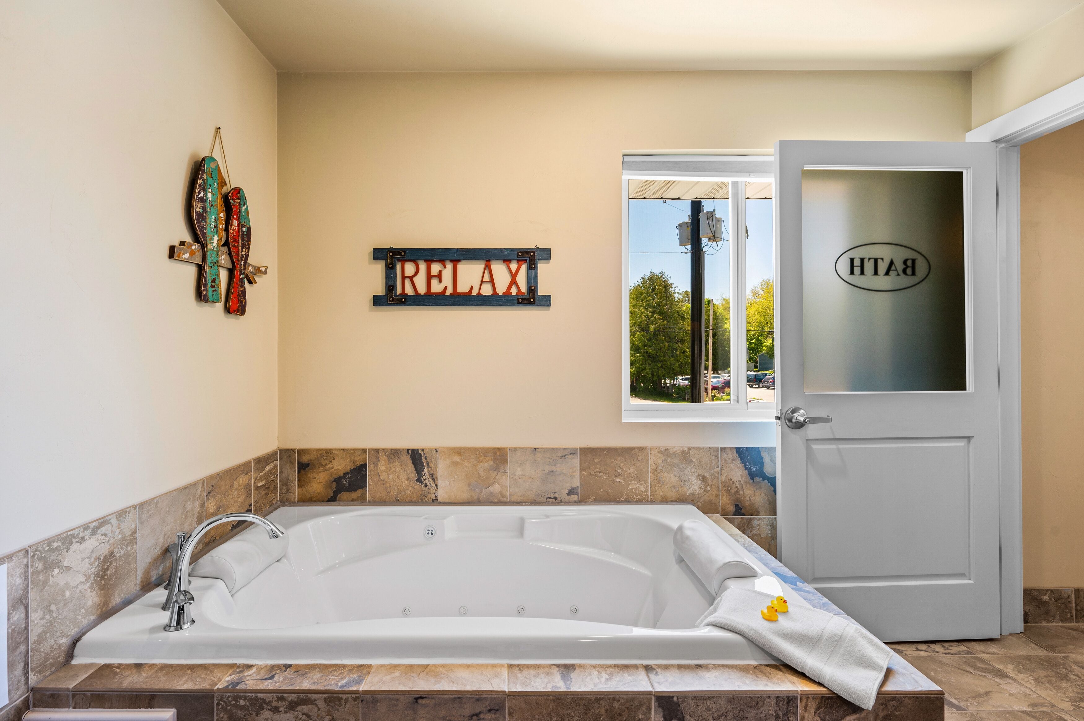 Un baño moderno con una bañera amplia, un cartel que dice 'RELAX' y una puerta con un ventanal de vidrio esmerilado.