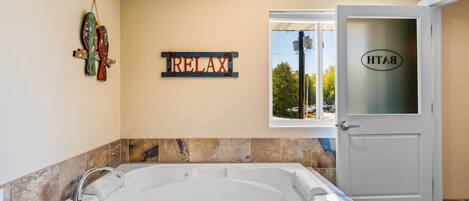 Un baño moderno con una bañera amplia, un cartel que dice 'RELAX' y una puerta con un ventanal de vidrio esmerilado.