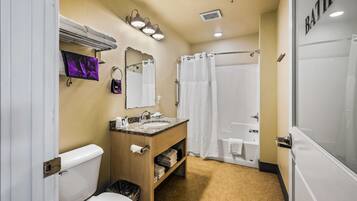A bathroom with a toilet, sink, vanity, mirror, shower curtain, and a bathtub.