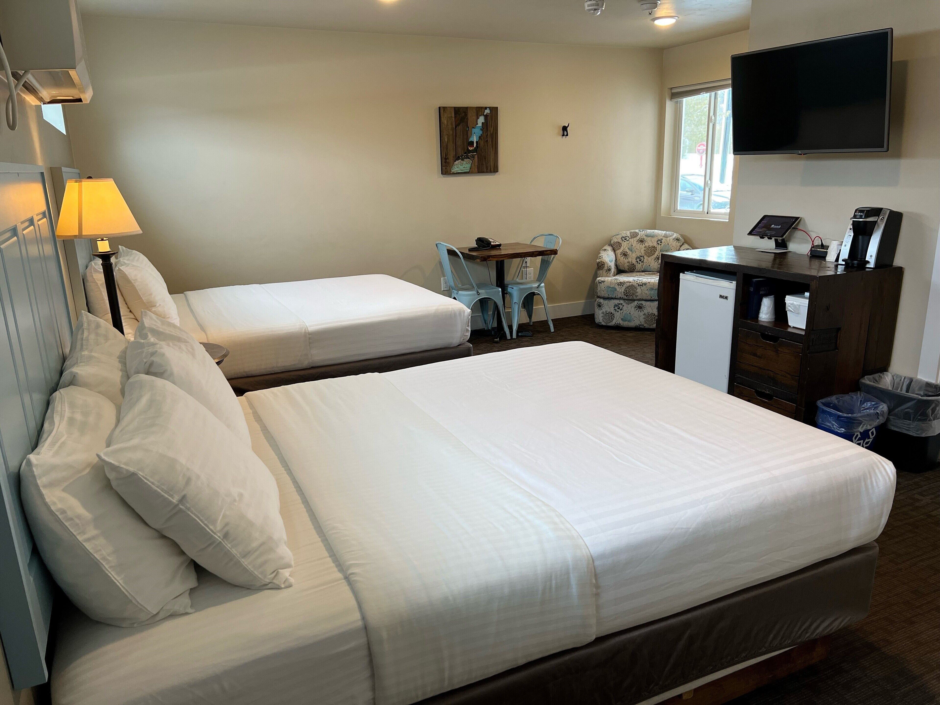 Een hotelkamer met twee bedden, een bureau, een stoel, een televisie en een prullenbak.