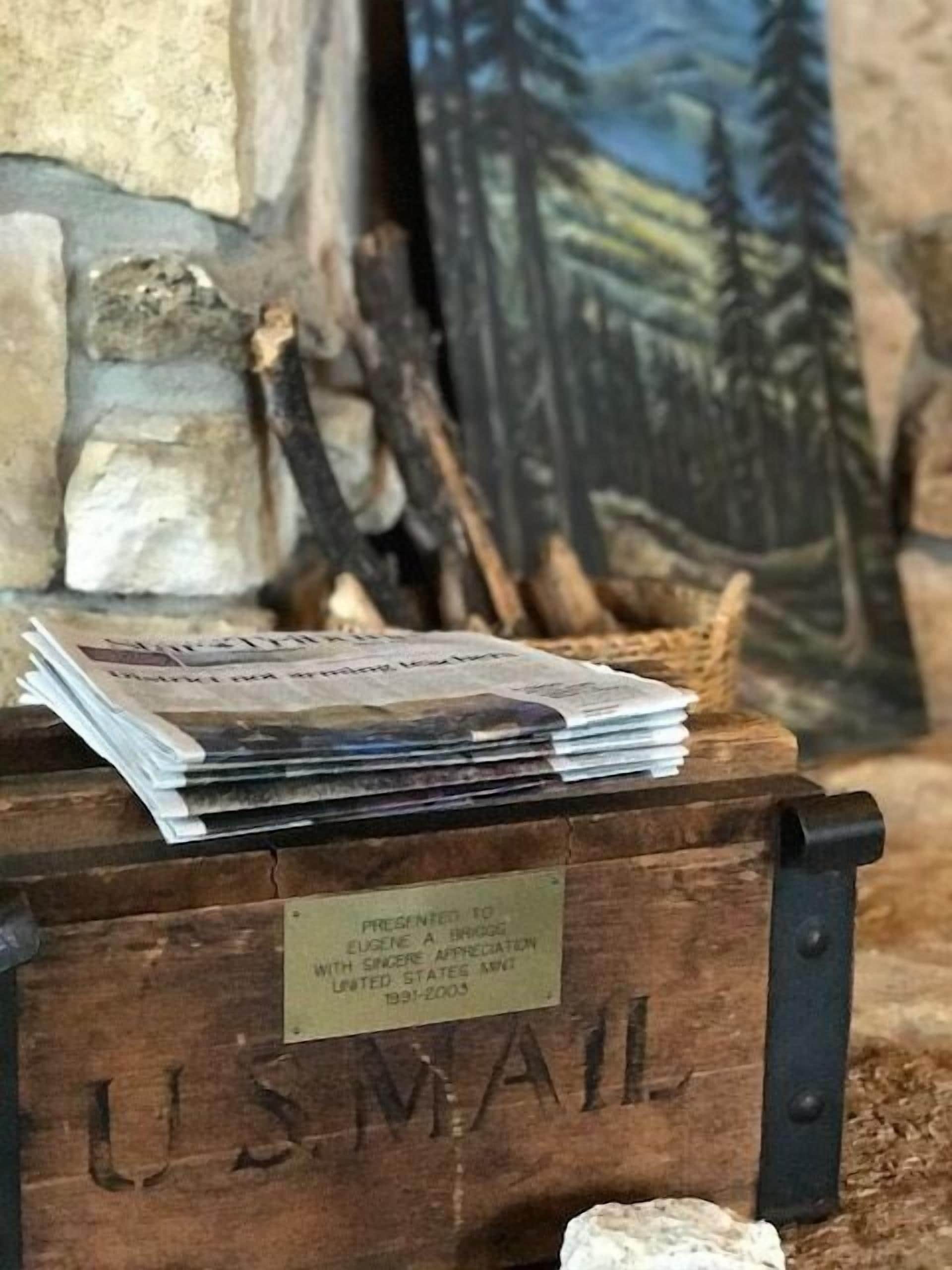 A wooden box labeled "U.S. Mail" with a stack of newspapers and a plaque indicating a presentation to Eugene A. Bridges with the United States Mint from 1991-2003.