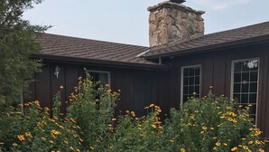 A building with a stone chimney, a dark brown exterior, and a garden with yellow flowers. - Bunkhouse Motel (Guernsey)