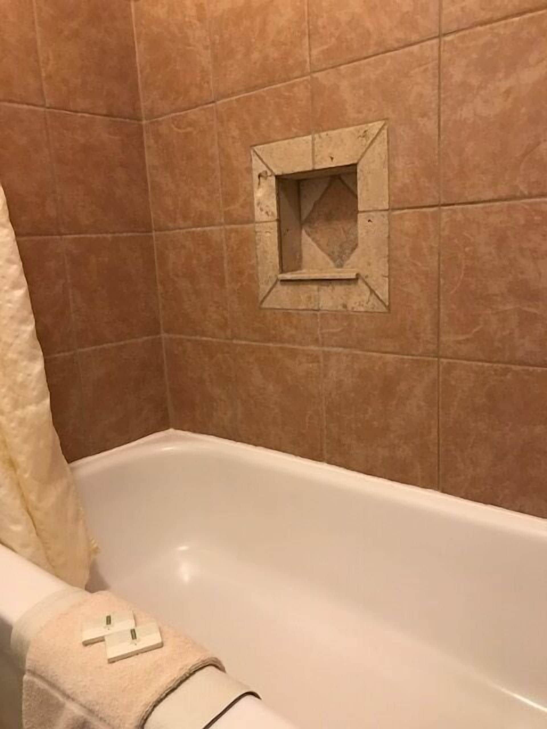 Un bagno con una vasca, un asciugamano e una piccola griglia quadrata a parete.