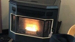 A room with a black wood-burning stove, a patterned rug, and a black hat on a chair. - Bunkhouse Motel (Guernsey)