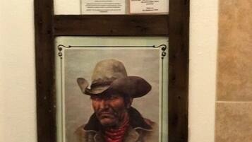 A framed portrait of a person in a cowboy hat and coat hanging on a wall above a toilet.