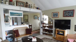 A living room with a sofa, a coffee table, a television, and a bookshelf. - Otter Creek Inn (Mount Desert)