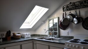 A kitchen with a skylight, a stove, and hanging pots. - Otter Creek Inn (Mount Desert)