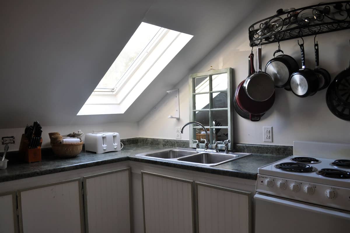 A kitchen with a skylight, a stove, and hanging pots.