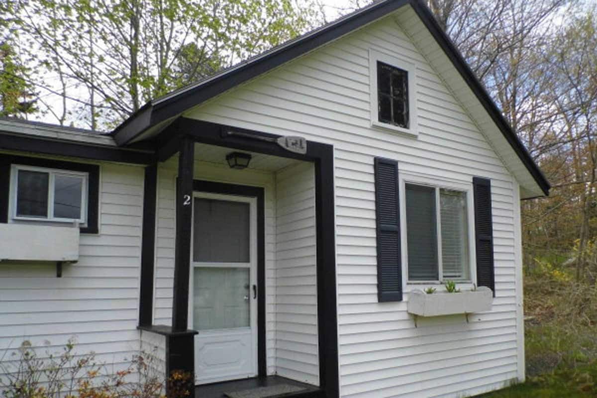 A two-story house with a white exterior and black trim. There is a front door with a glass panel, a small porch, and a window with shutters.