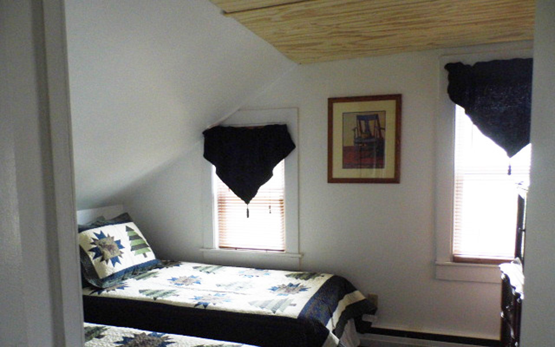 A bedroom with a bed, a window with blinds, a framed picture on the wall, and a wooden ceiling.