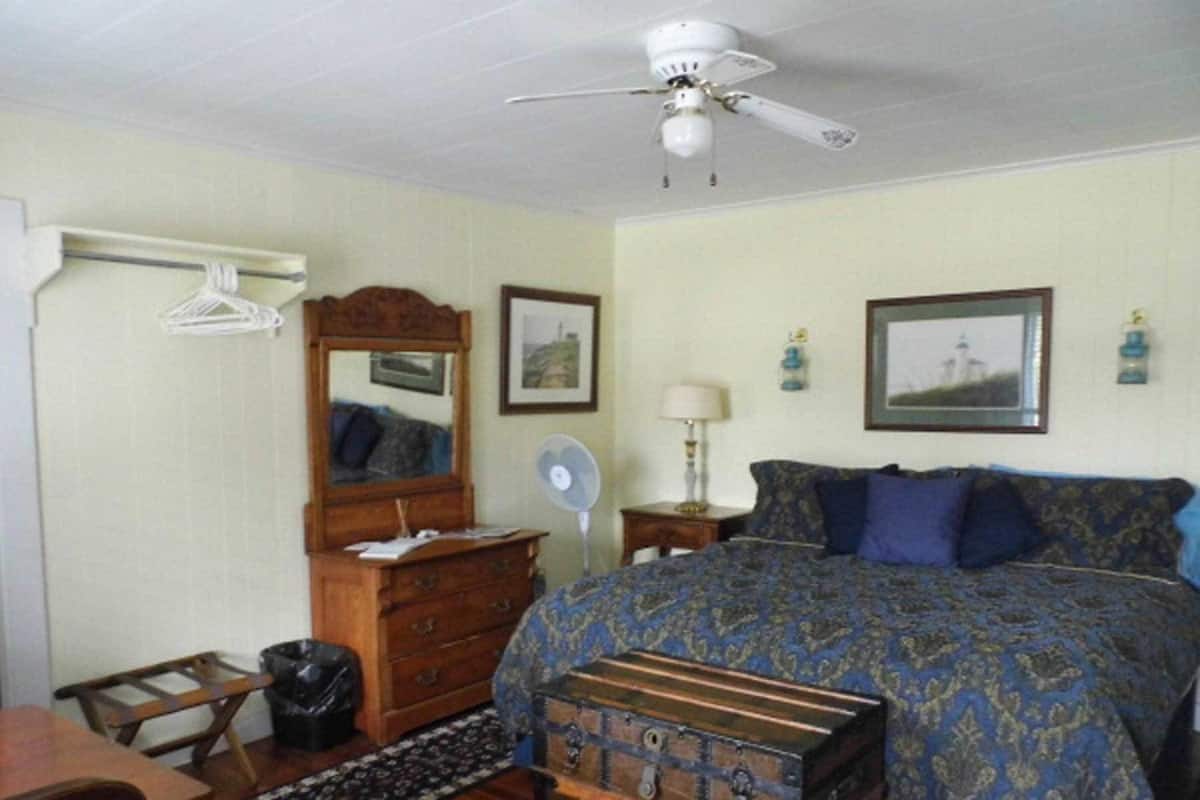A bedroom with a bed, dresser, mirror, ceiling fan, and two wall-mounted fans.