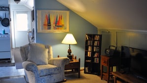 A living room with a floral armchair, a lamp, a bookshelf, and a television. - Otter Creek Inn (Mount Desert)