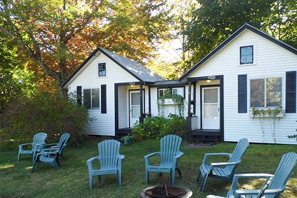 A two-story house with a porch and several Adirondack chairs in the yard.