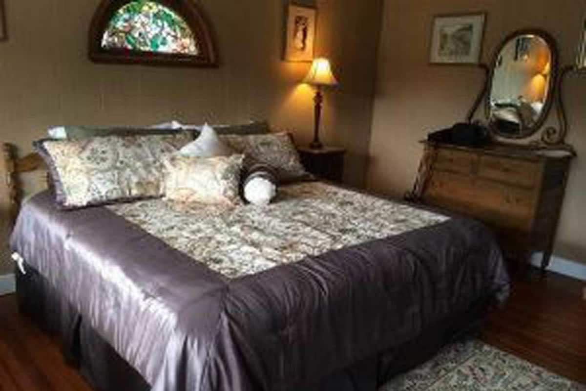 A bedroom with a bed, a nightstand, a dresser, and a mirror.