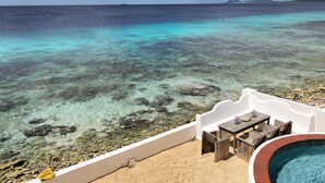 Una vista despejada del océano, una playa arenosa y un área de piscina con mesa y sillas.